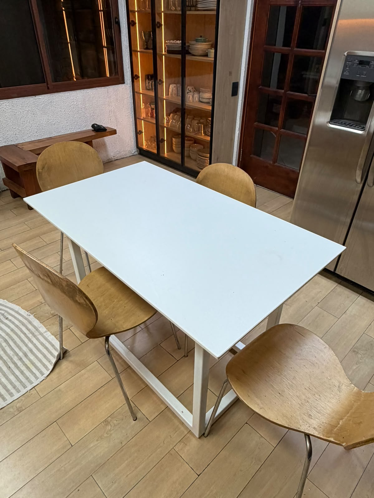 Comedor blanco con sillas de madera curva junto a vitrina iluminada